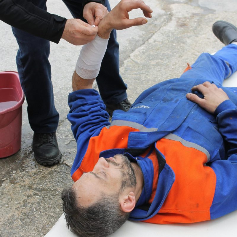 Injured worker receiving first aid on-site with arm bandage applied.